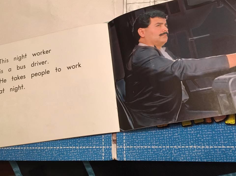 Full first-grade reader spread showing a bus driver resembling Saddam Hussein