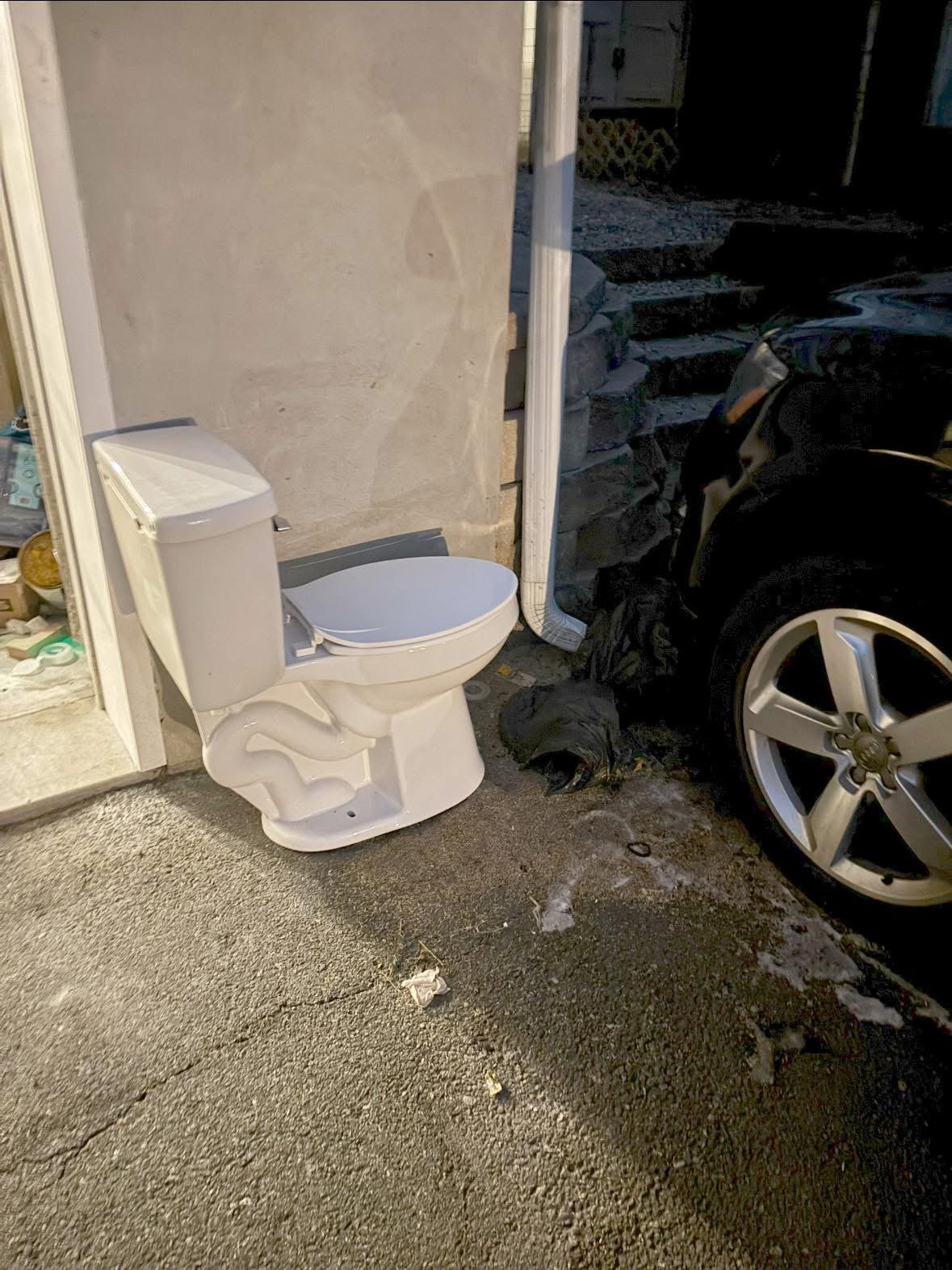 Outdoor toilet beside garage and parked car